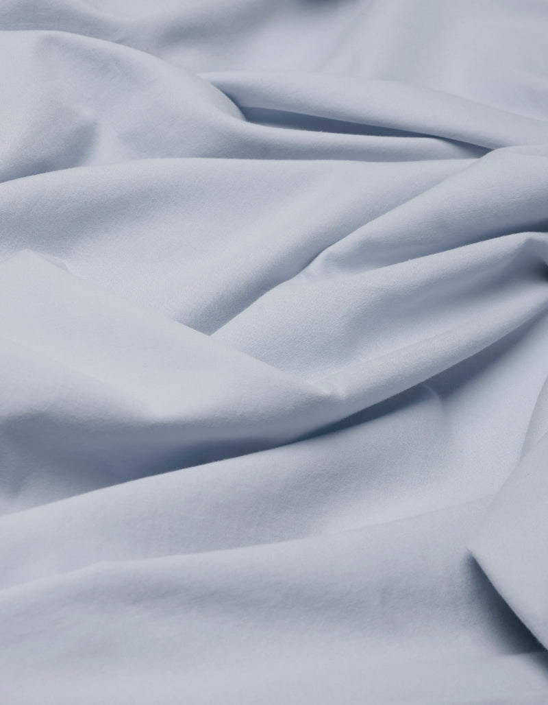 The Cozy Earth Soft-Wash Cotton Flat Sheet features a soft, light blue fabric with gentle folds and creases for a smooth, flowing texture.
