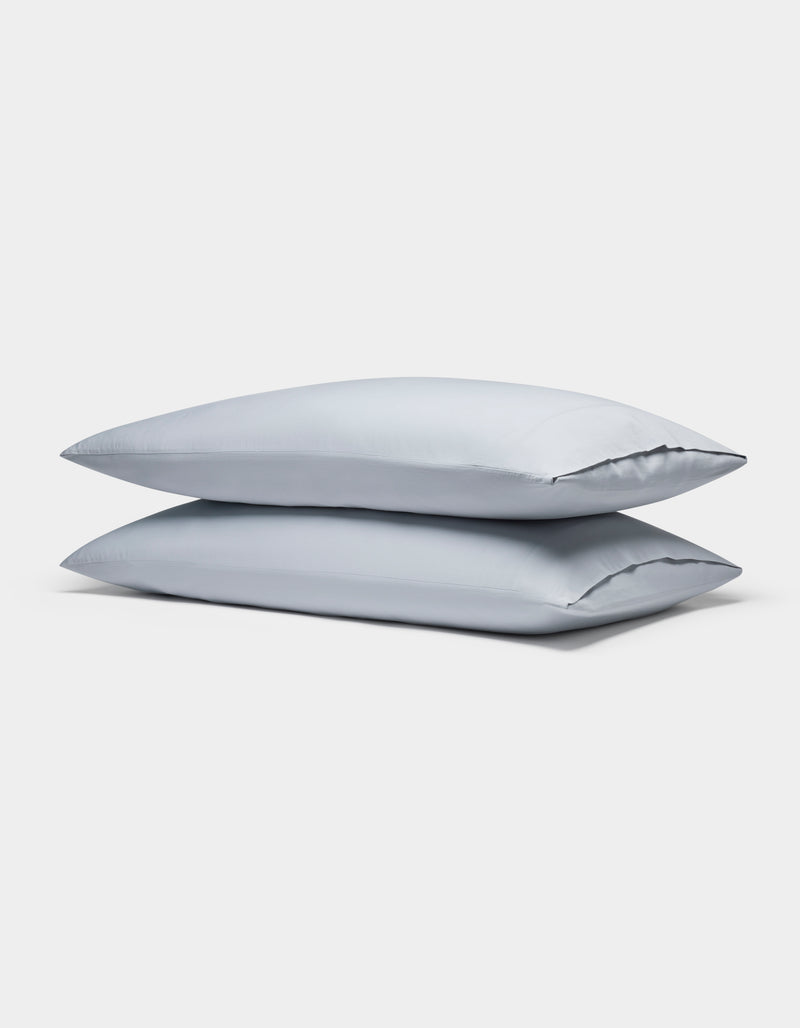 Two Soft-Wash Cotton Pillowcases by Cozy Earth, in light gray, are neatly stacked against a plain white background.