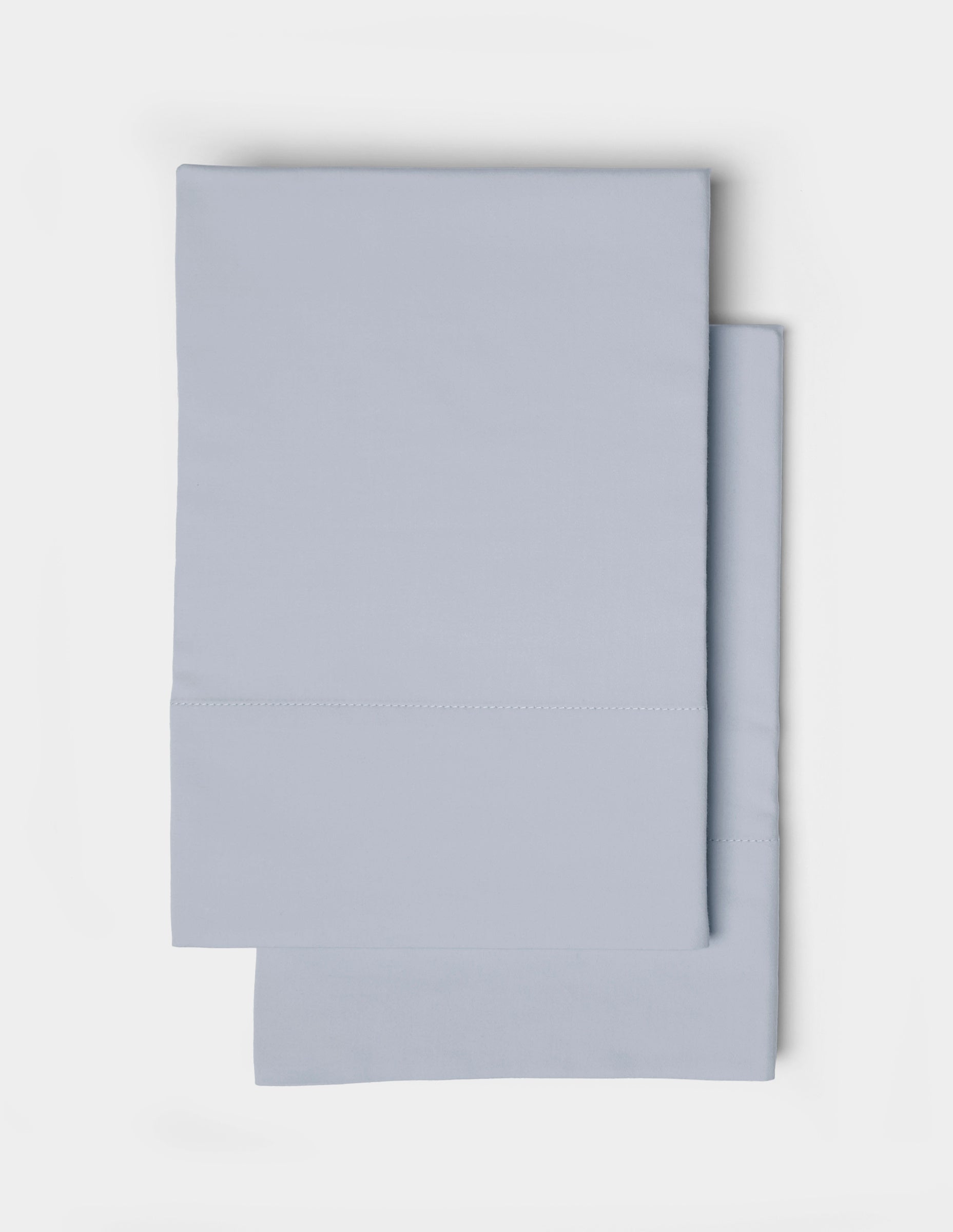 Two neatly folded Soft-Wash Cotton Pillowcases by Cozy Earth, in light blue, are stacked on top of each other against a white background.|Color:Shore
