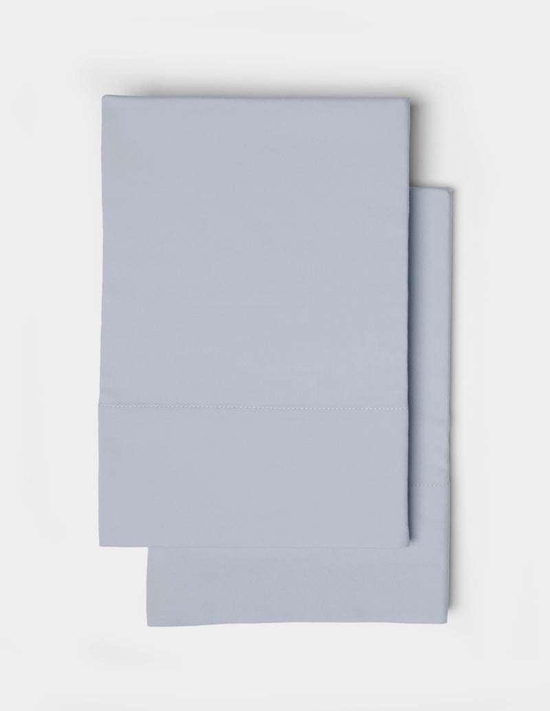 Two neatly folded Soft-Wash Cotton Pillowcases by Cozy Earth, in light blue, are stacked on top of each other against a white background.