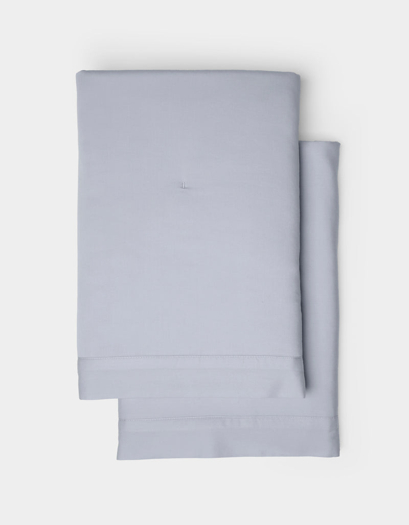 Two Soft-Wash Cotton Quilted Shams by Cozy Earth, in a light gray hue, are neatly folded and stacked on a plain white background.