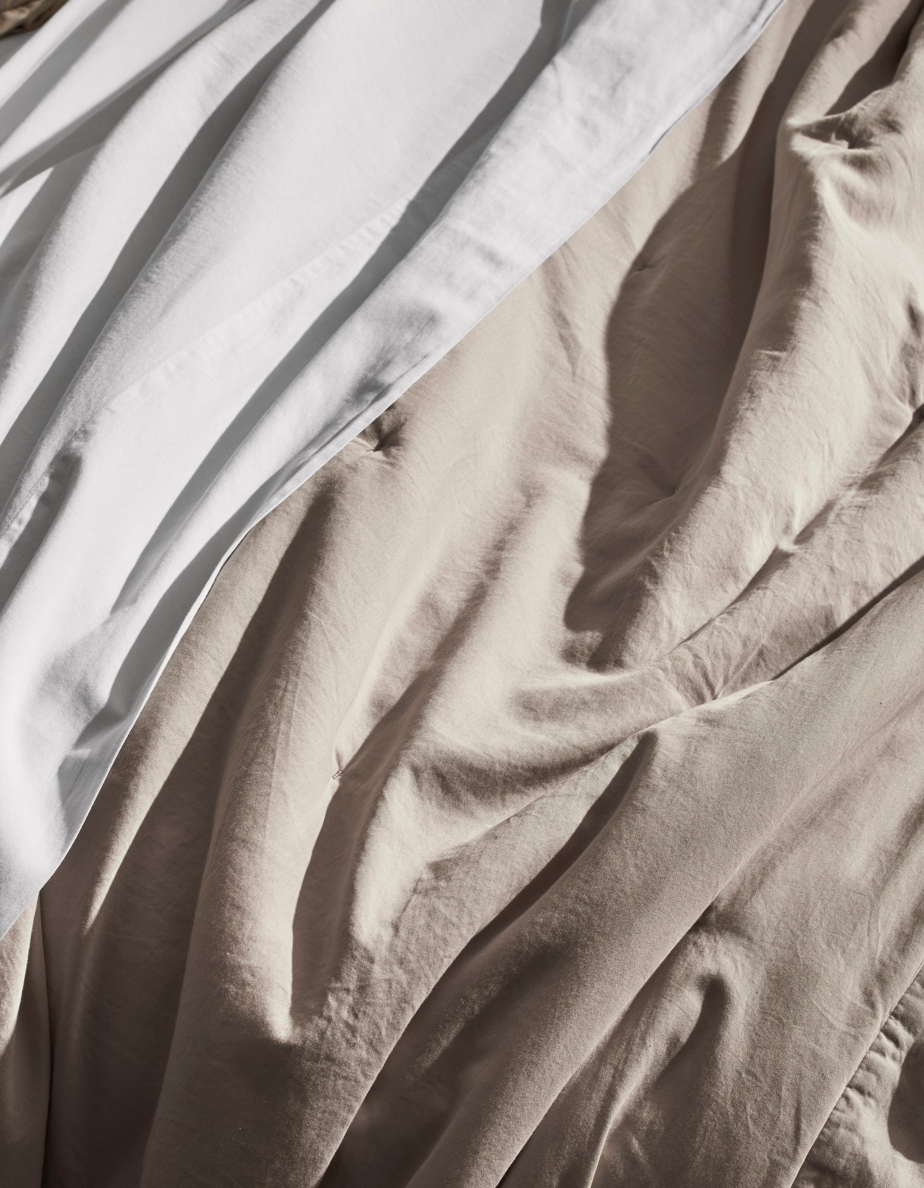 A close-up of the Cozy Earth Soft-Wash Cotton Quilt, showcasing its white and beige tones with gentle, natural light highlighting the soft texture and elegant folds.