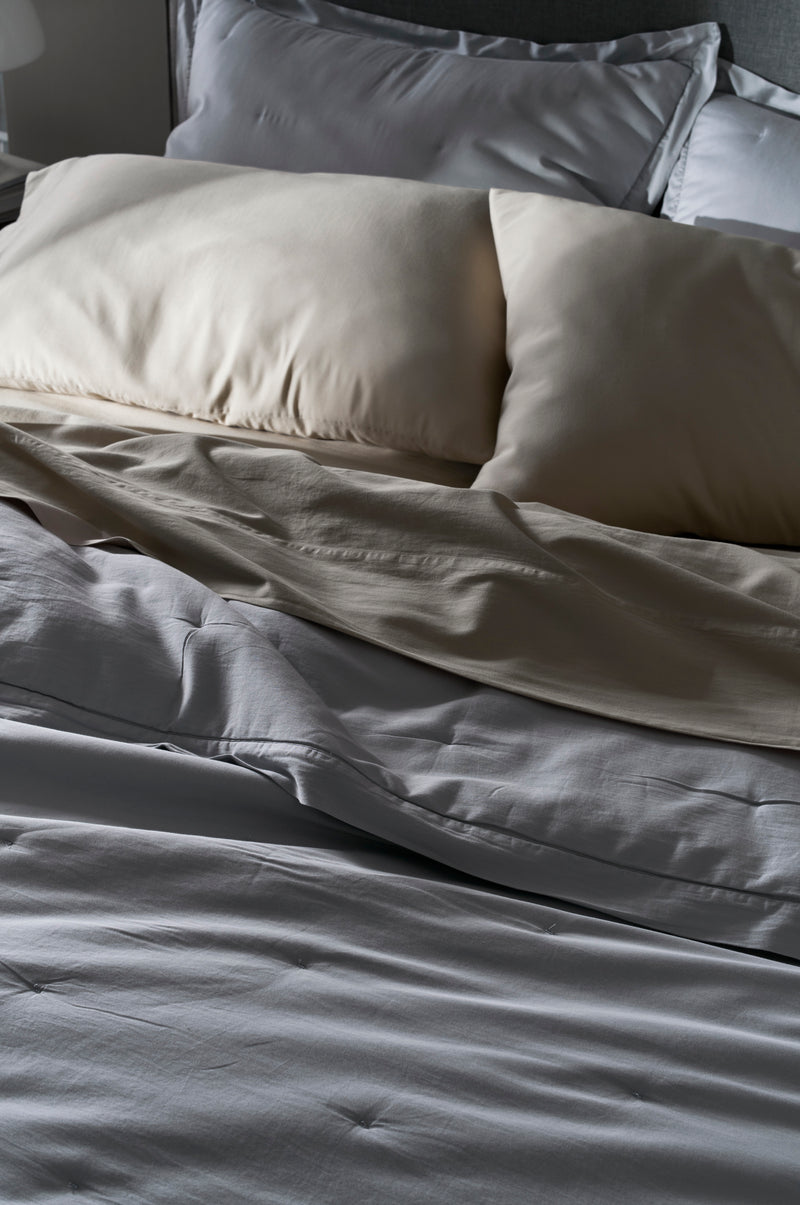 A close-up of an unmade bed features the Cozy Earth Soft-Wash Cotton Quilt with light-colored sheets and two cream pillows, creating a cozy and relaxed vibe with its gently rumpled appearance.