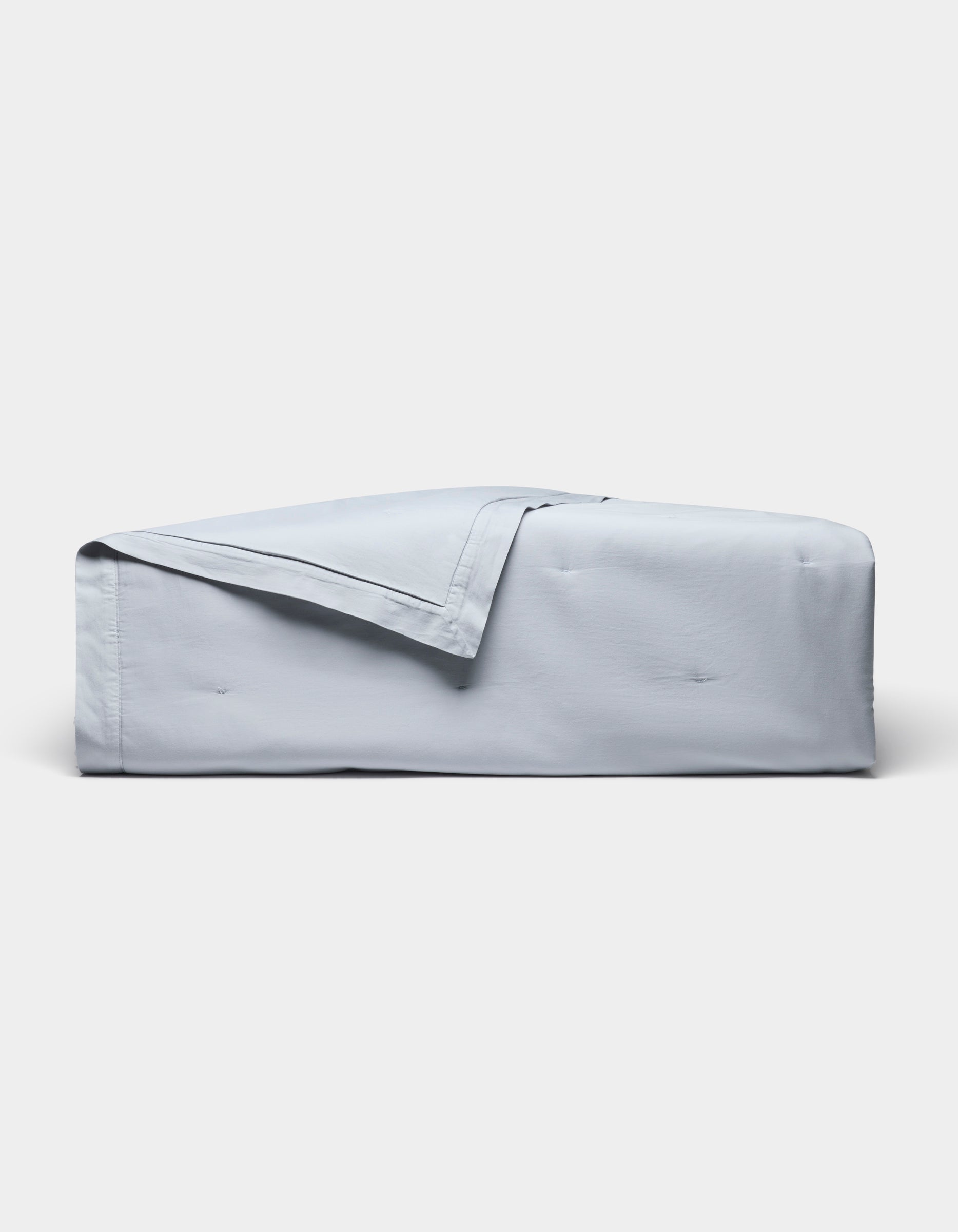 The Cozy Earth Soft-Wash Cotton Quilt Bundle, in light blue, is neatly folded and draped over a rectangular surface against a plain white background.