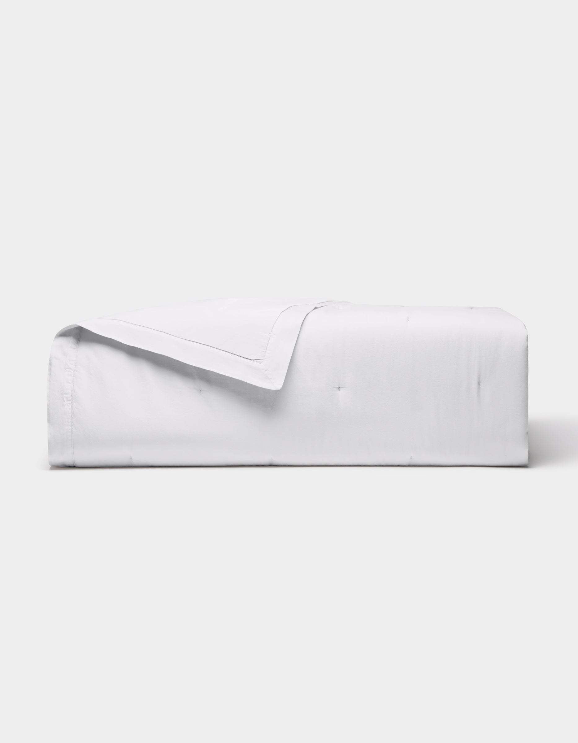 The Cozy Earth Soft-Wash Cotton Quilt is neatly folded with one corner turned down, showcased against a plain light gray background.|Color:White