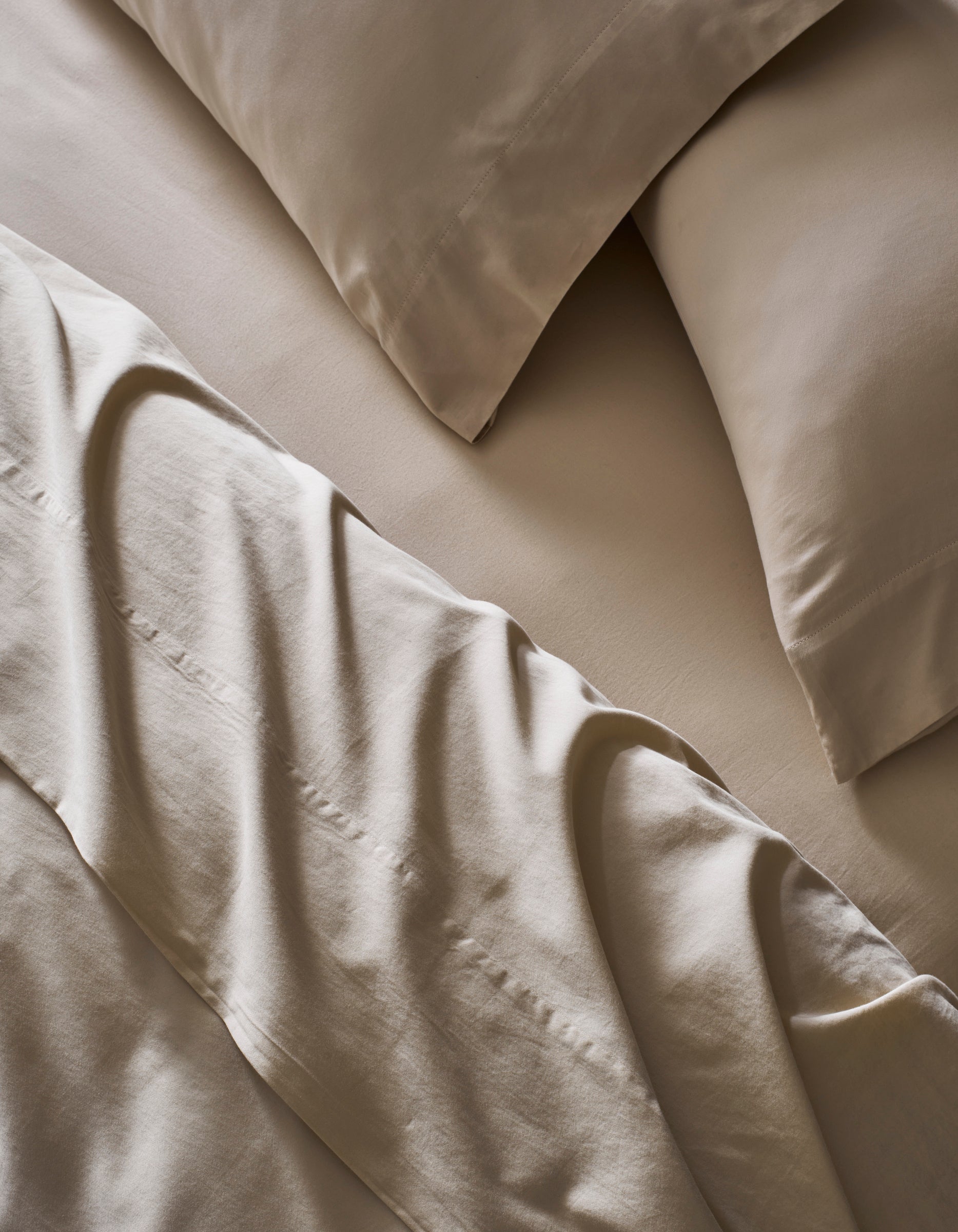 A close-up of a bed made with Cozy Earth’s Soft-Wash Cotton Bedding Deluxe Bundle – Down Alternative shows smooth beige sheets and pillowcases, giving the room a calm and inviting vibe.