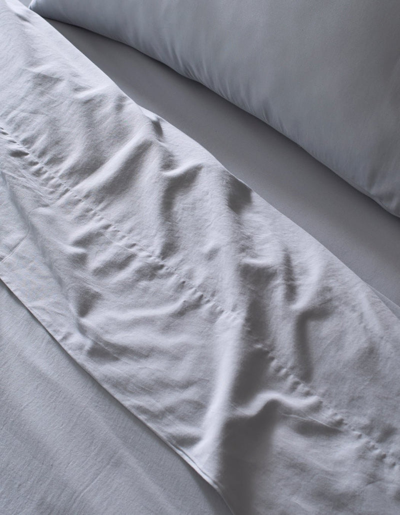 Close-up of a neatly made bed featuring Cozy Earth's Soft-Wash Cotton Sheet Set in light grey. Slight wrinkles add texture to the soft, clean fabric, giving the bedding an inviting look.