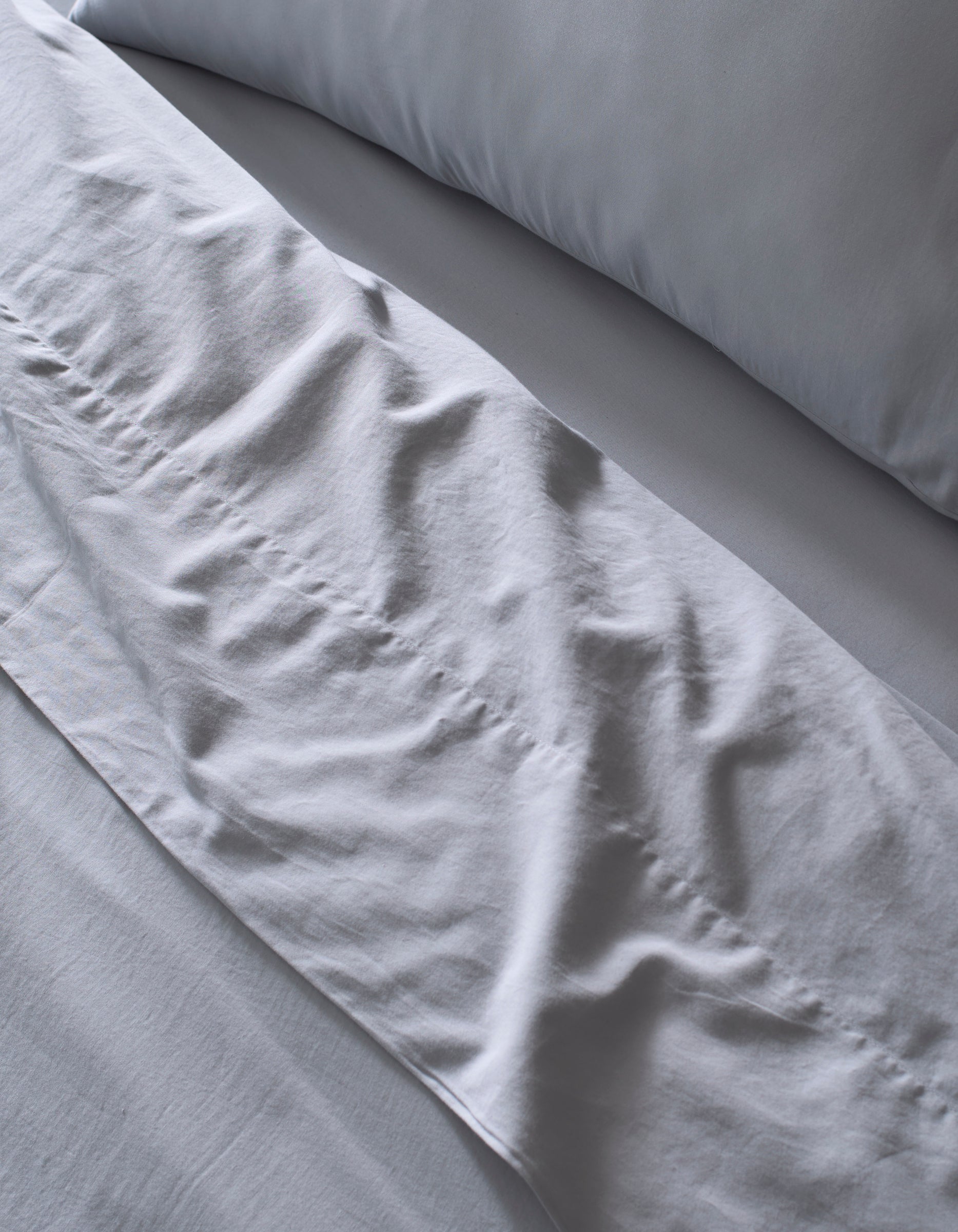 Close-up of a neatly made bed featuring the Cozy Earth Soft-Wash Cotton Bedding Core Bundle in light gray, with softly wrinkled sheets and pillowcase hinting at recent use or adjustment.