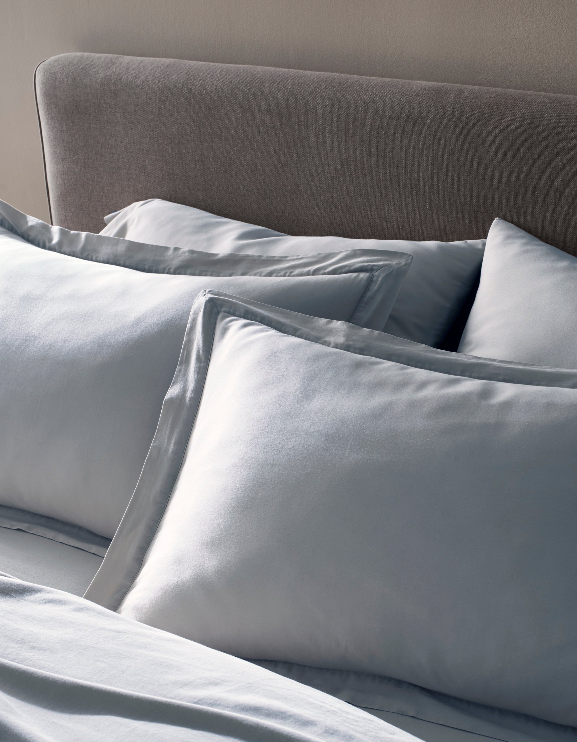 Two Soft-Wash Cotton Shams by Cozy Earth in light blue rest against a gray upholstered headboard, paired with coordinated bedding to create a calm and inviting bedroom setting.