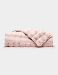 The Bubble Cuddle Blanket by Cozy Earth, in pale pink faux fur, is shown folded on a light gray background with one corner draped to reveal its soft texture.|Color:Blossom