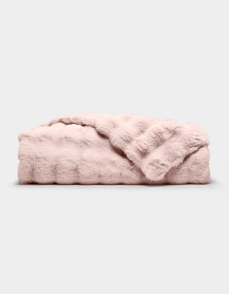 The Bubble Cuddle Blanket by Cozy Earth, in pale pink faux fur, is shown folded on a light gray background with one corner draped to reveal its soft texture.