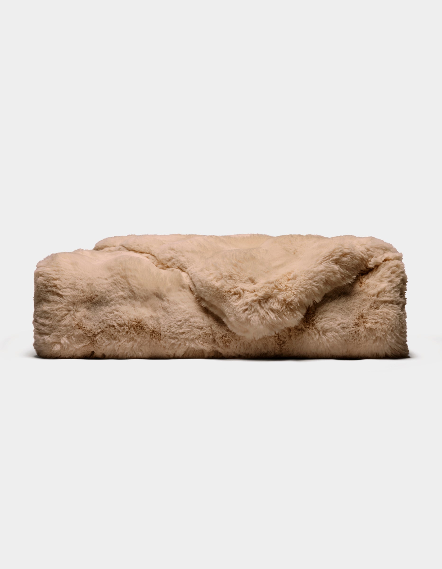 The Double Bubble Cuddle Blanket by Cozy Earth, a rectangular beige faux fur throw, rests on a plain white background with one corner of the plush fur softly folded over the top.