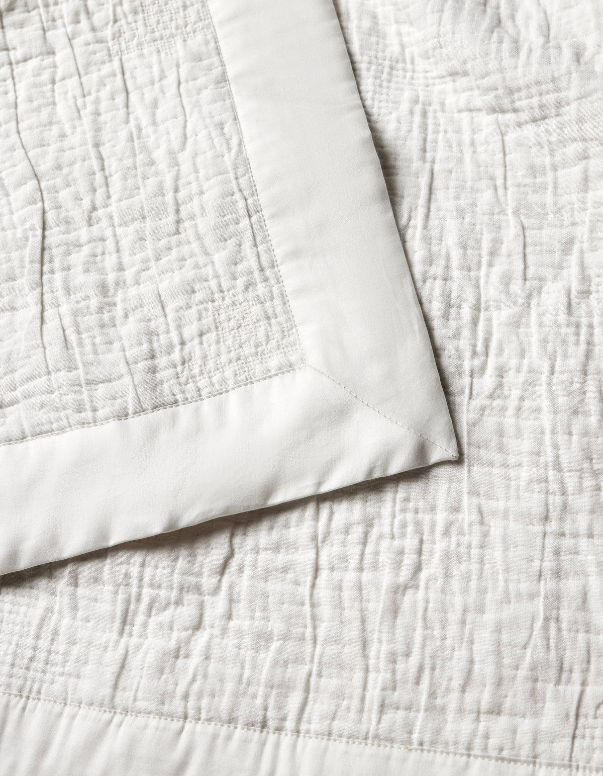 The Cozy Earth Little Bee Matelasse Baby Blanket features a cream hue, textured stitched pattern, and smooth solid border. A folded corner highlights both the elegant surface and refined edging.