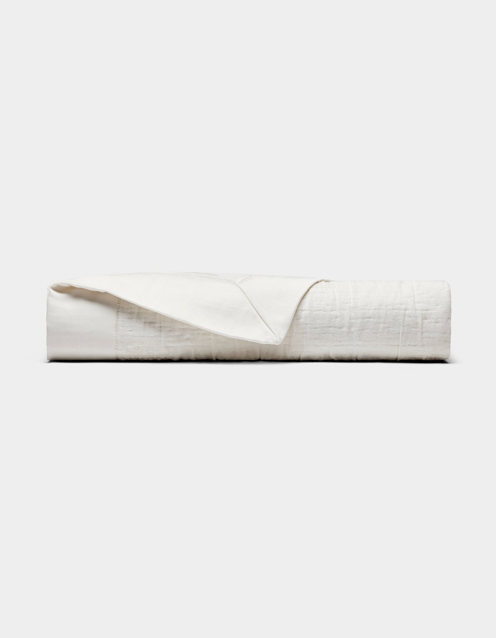 The Cozy Earth Little Bee Matelasse Baby Blanket, in white, is neatly folded with one corner partially flipped over and displayed against a plain light gray background.