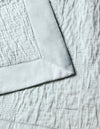 Close-up of the Cozy Earth Little Bee Matelasse Baby Blanket in light gray, showcasing its soft, textured fabric, visible stitched patterns, and a smooth satin border.|Color:Vapor
