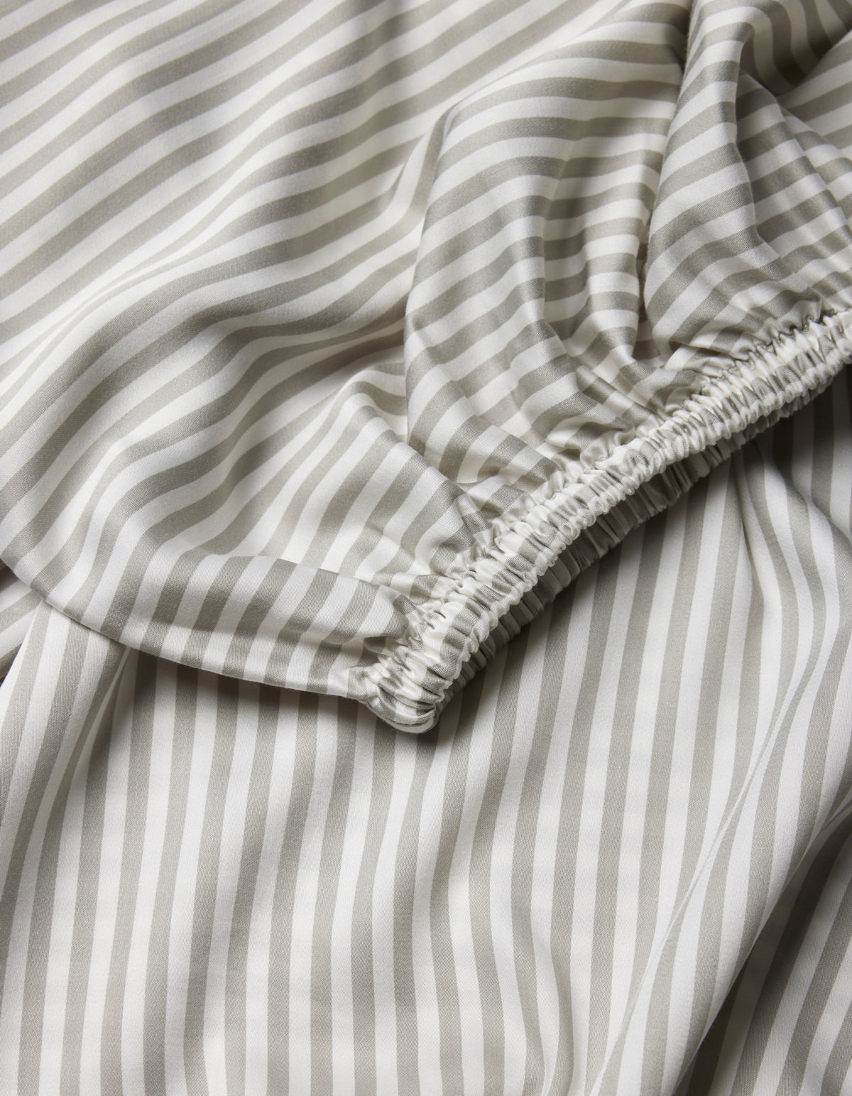 A close-up of Cozy Earth's Bamboo Fitted Sheet, showcasing light fabric with beige and white vertical stripes and a gathered, elasticized seam.