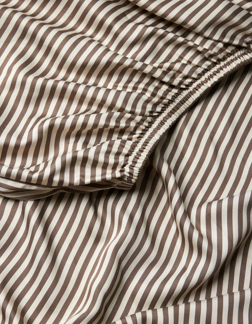 Close-up of Cozy Earth Bamboo Fitted Sheet, showcasing brown and white vertical stripes with a gathered, elasticized section and a smooth, flowing texture.