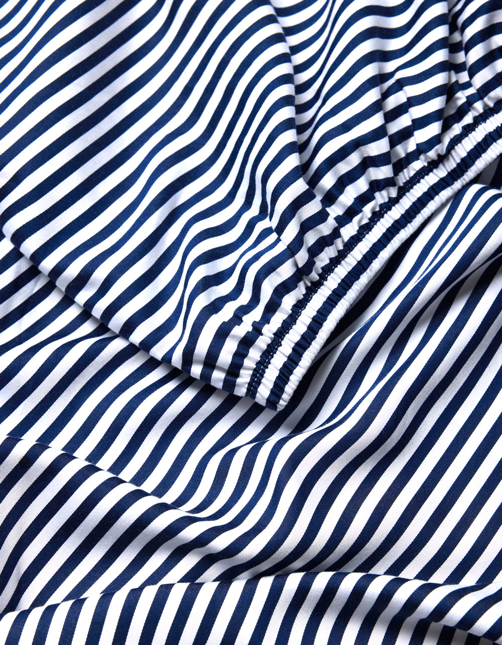 A close-up of the Cozy Earth Bamboo Fitted Sheet shows its navy blue and white stripes, with elasticized sections that gather the fabric into soft folds and curves.