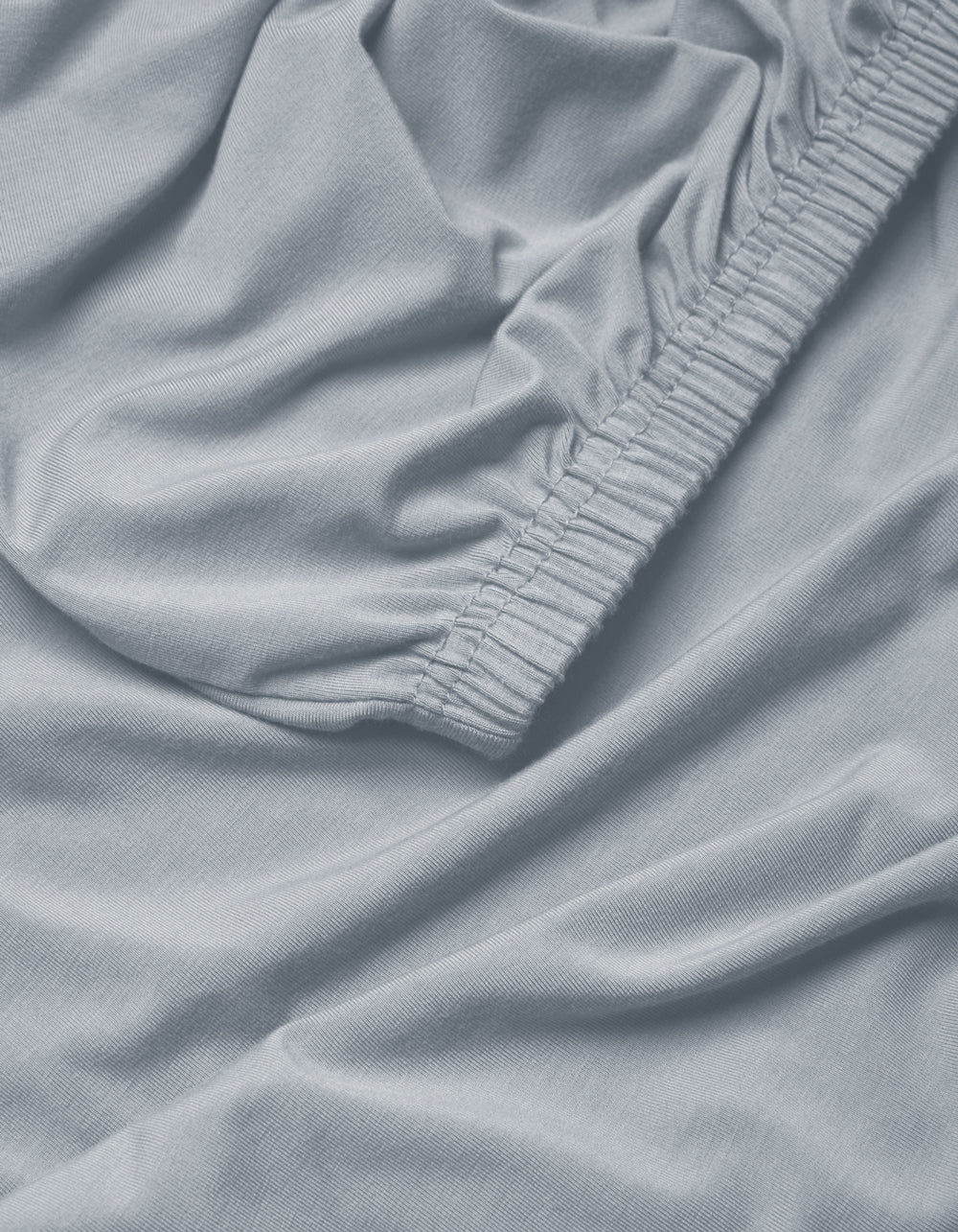 Close-up of Cozy Earth's Bamboo Jersey Fitted Sheet in light blue, featuring gathered elastic edges and a soft, slightly wrinkled fabric texture.