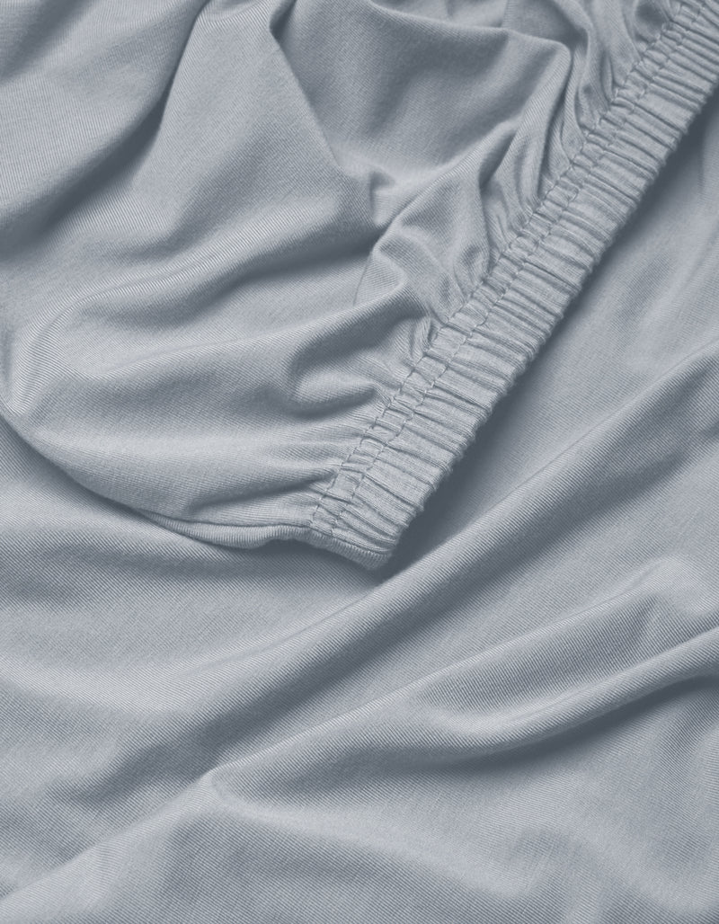 Close-up of Cozy Earth's Bamboo Jersey Fitted Sheet in light blue, featuring gathered elastic edges and a soft, slightly wrinkled fabric texture.