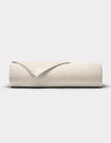 A neatly rolled Bamboo Jersey Flat Sheet by Cozy Earth in light beige rests on a plain, light gray background, with one edge partially folded over the roll to reveal its finished seam.|Color:Birch