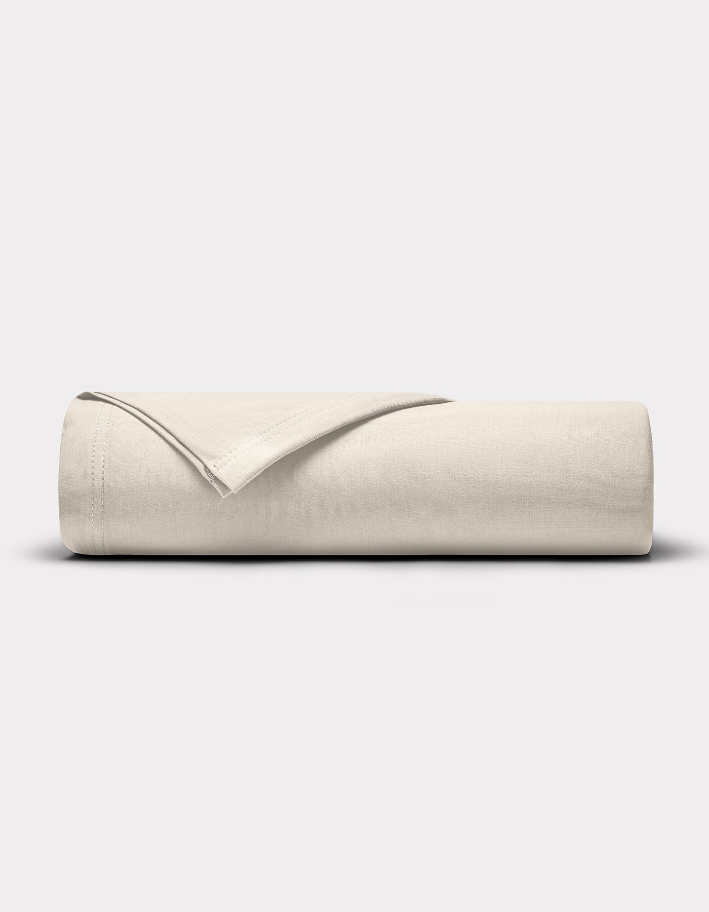 A neatly rolled Bamboo Jersey Flat Sheet by Cozy Earth in light beige rests on a plain, light gray background, with one edge partially folded over the roll to reveal its finished seam.|Color:Birch