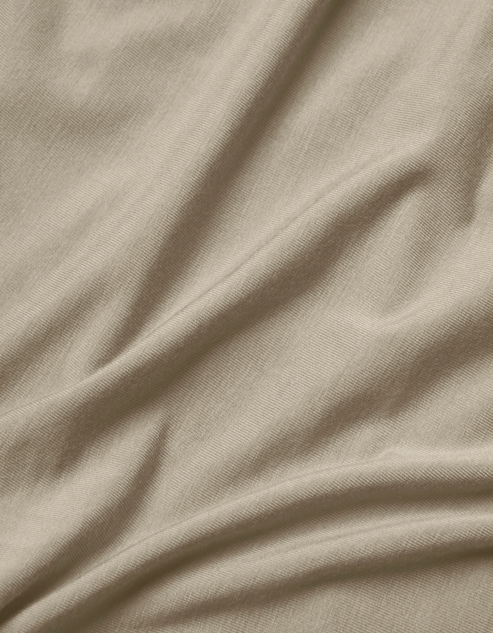 Close-up of Cozy Earth's Bamboo Jersey Flat Sheet in light beige, featuring soft, natural folds, gentle shadows, a smooth texture, and a subtle weave pattern.