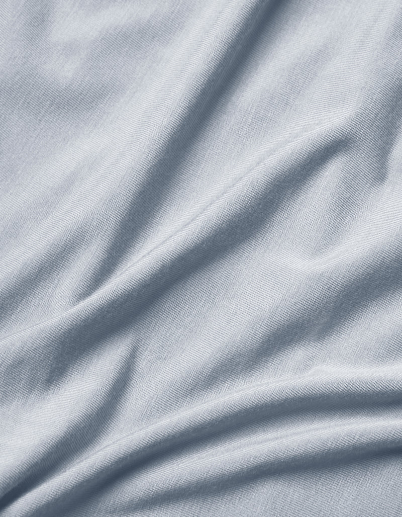Close-up of Cozy Earth Bamboo Jersey Flat Sheet in light grey or pale blue, featuring soft folds, subtle texture, and gentle shadows and highlights.