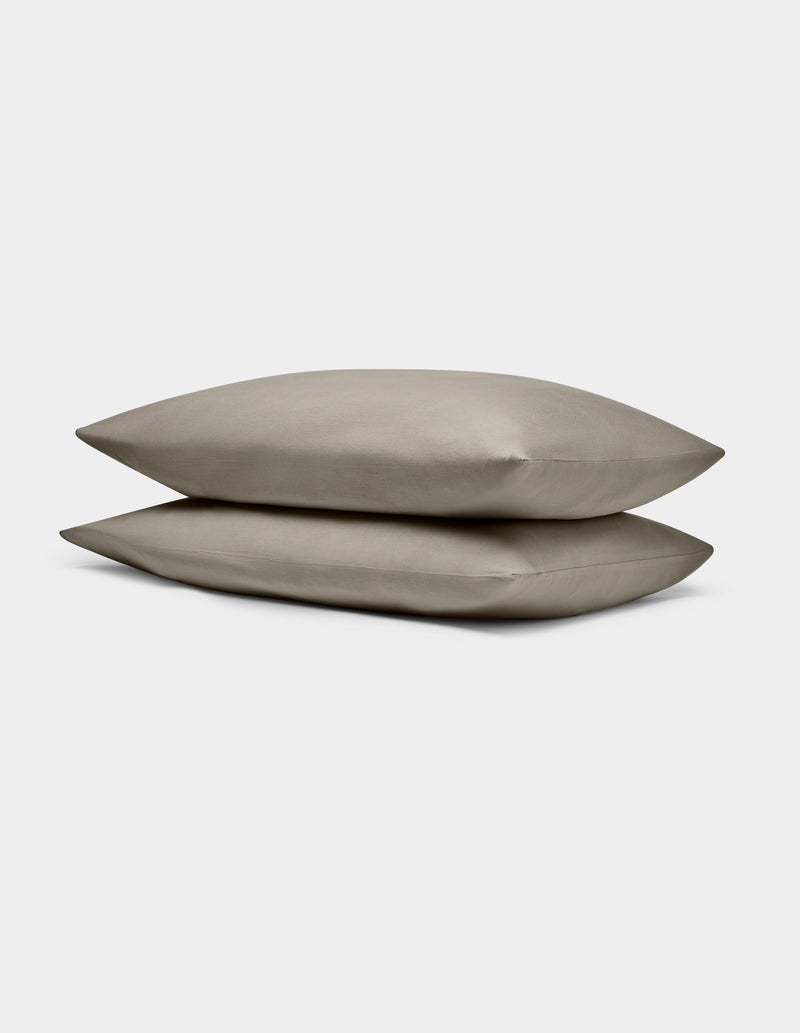 Two Cozy Earth Bamboo Jersey Pillowcases in taupe are stacked atop each other against a plain, light gray background.