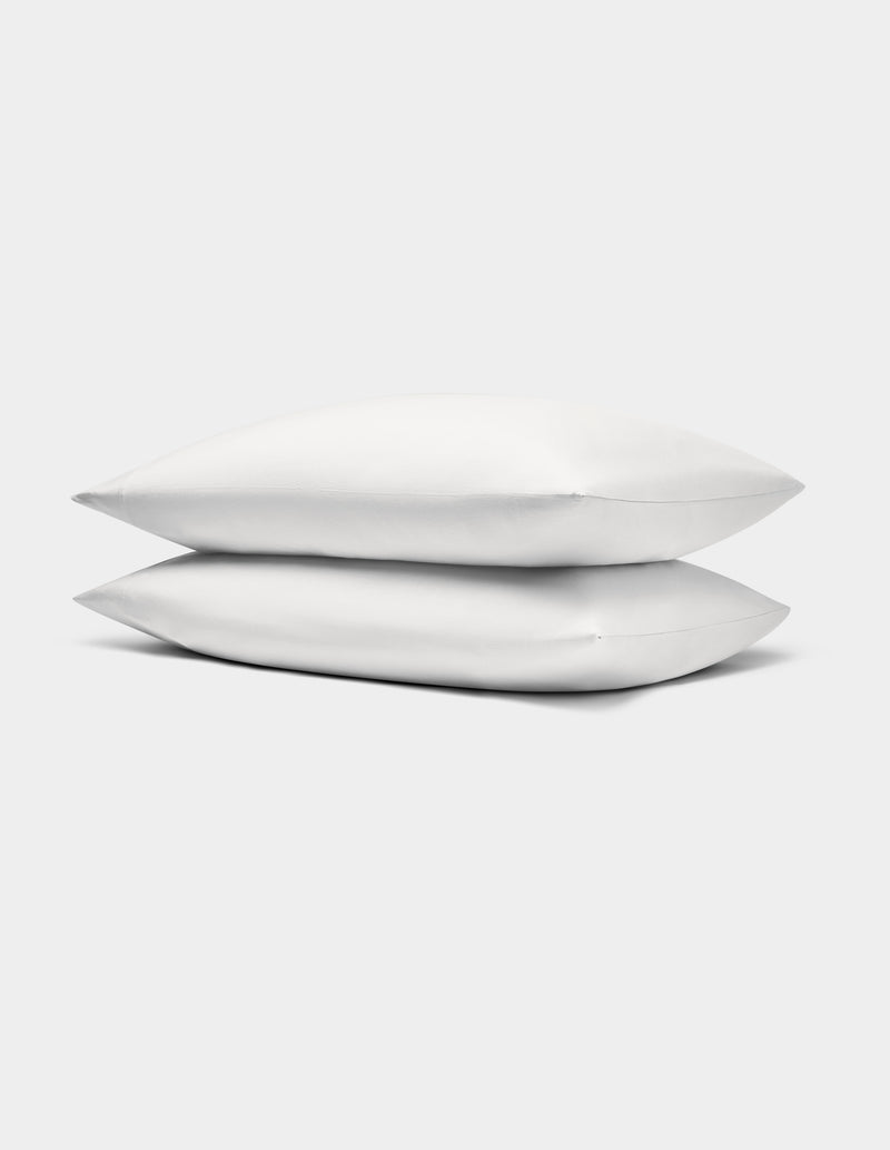 Two Bamboo Jersey Pillowcases by Cozy Earth, in white, stacked neatly against a plain light gray background.