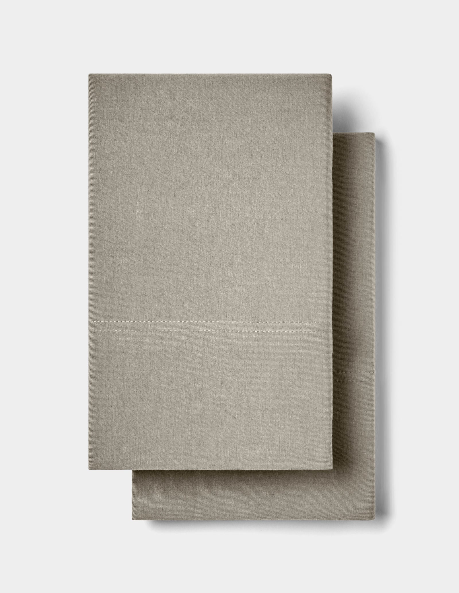 Two neatly folded, light beige Bamboo Jersey Pillowcases by Cozy Earth stacked on top of each other against a plain white background.