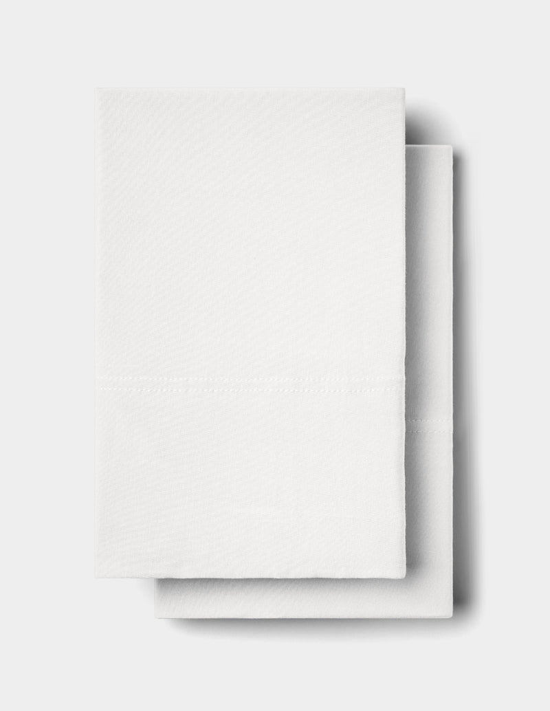 Two neatly folded Bamboo Jersey Pillowcases by Cozy Earth are stacked on a plain light gray surface, with one slightly overlapping the other. The pillowcases feature a subtle textured pattern and a visible horizontal crease line.