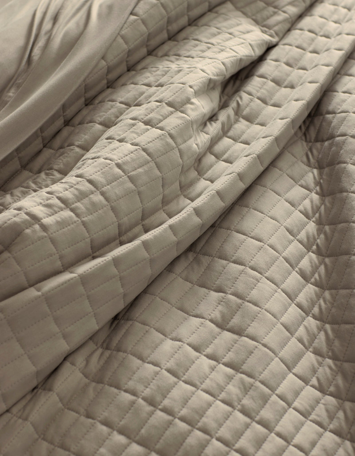 A close-up of the Cozy Earth Bamboo Jersey Quilt in beige, featuring a soft, quilted square pattern with gentle folds and visible texture.|Color:Driftwood