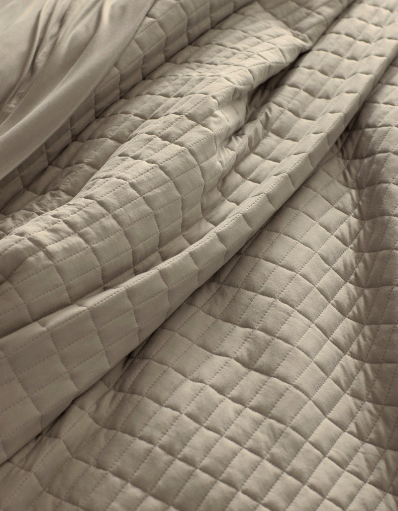 A close-up of the Cozy Earth Bamboo Jersey Quilt in beige, featuring a soft, quilted square pattern with gentle folds and visible texture.