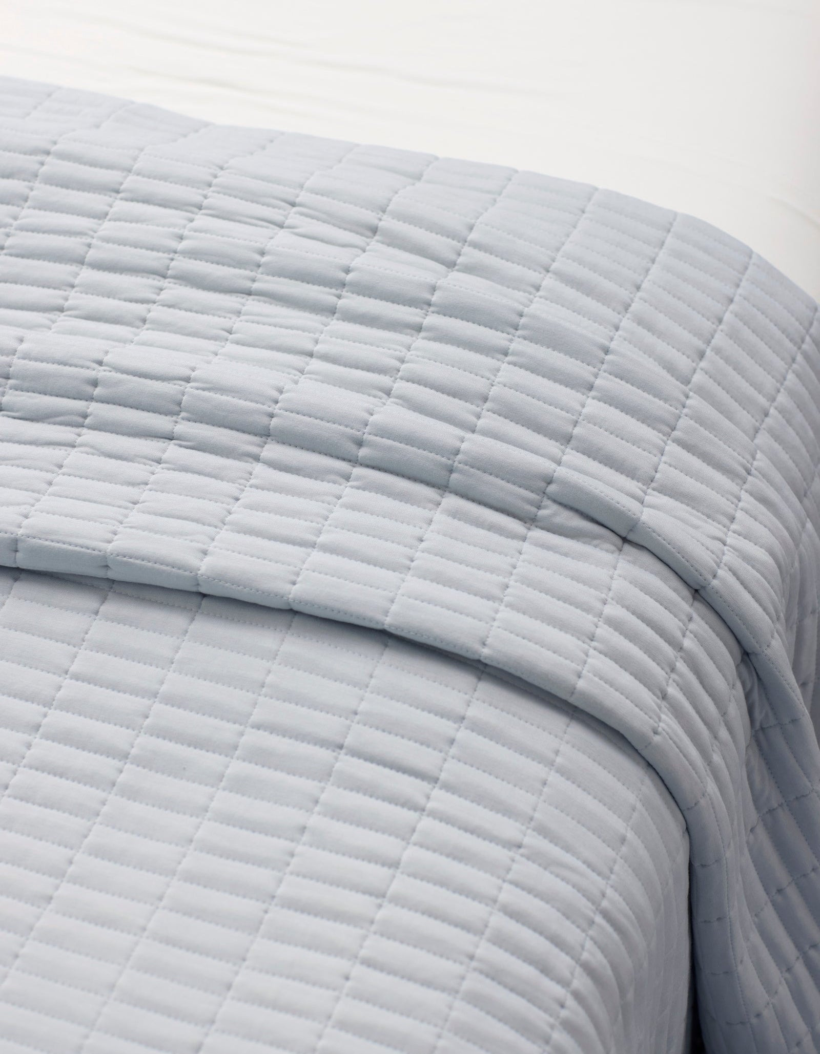 A close-up of a neatly made bed with the Cozy Earth Bamboo Jersey Quilt Bundle, featuring a light gray, square-patterned quilt layered over white sheets.