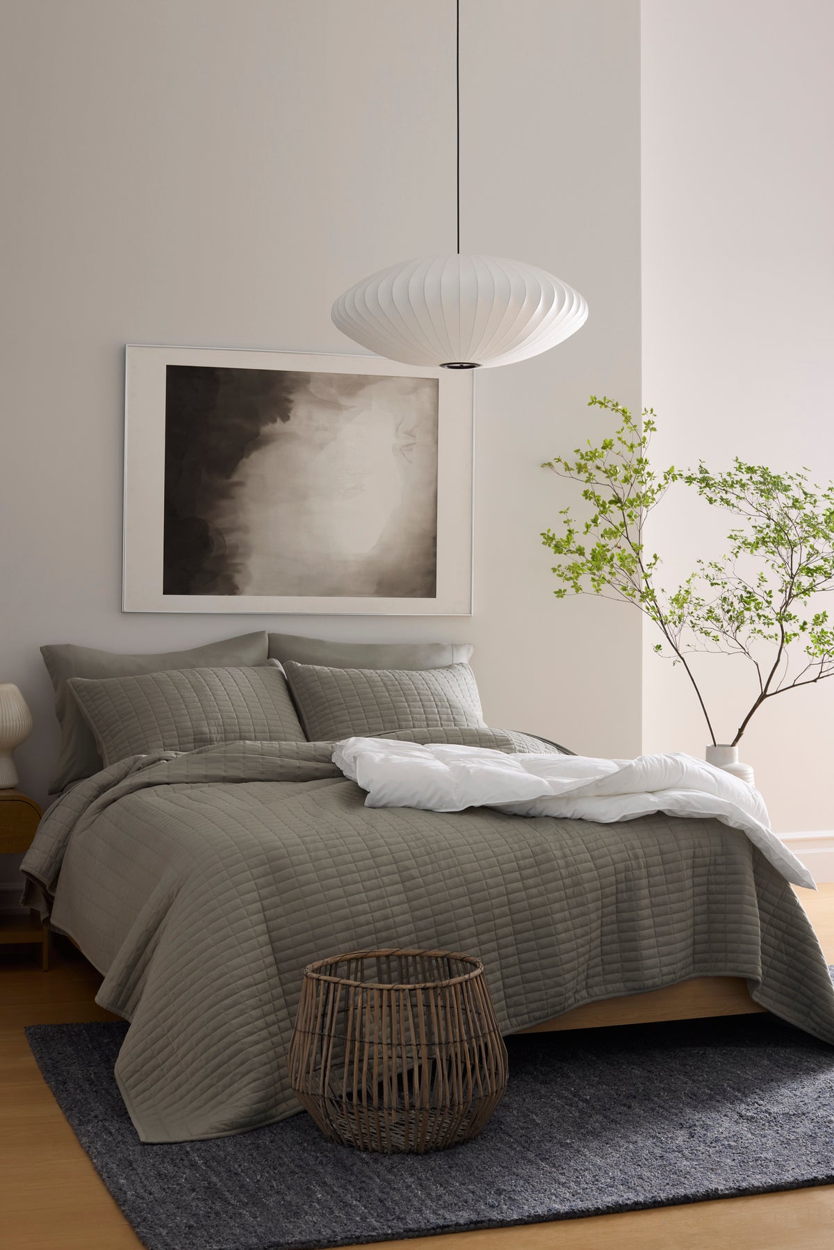 A neatly made bed features the Cozy Earth Bamboo Jersey Quilt in light pink with matching pillows, set against a wooden wall in a minimal, modern bedroom with neutral tones and simple decor.|Color:Petal