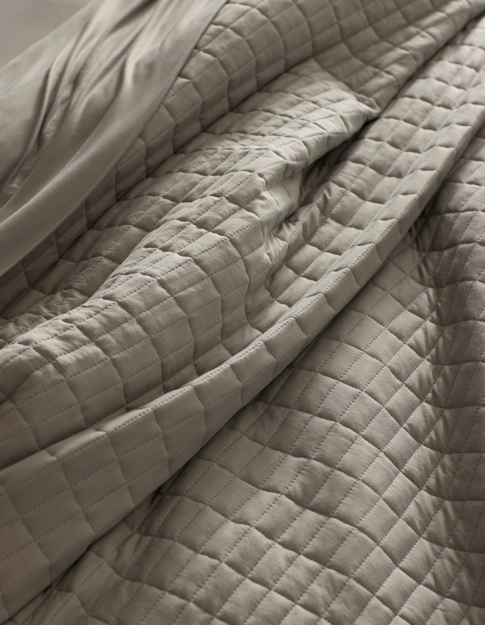 Close-up of the Cozy Earth Bamboo Jersey Quilt in light gray, featuring a quilted grid pattern with visible folds and soft texture for a cozy, inviting look.