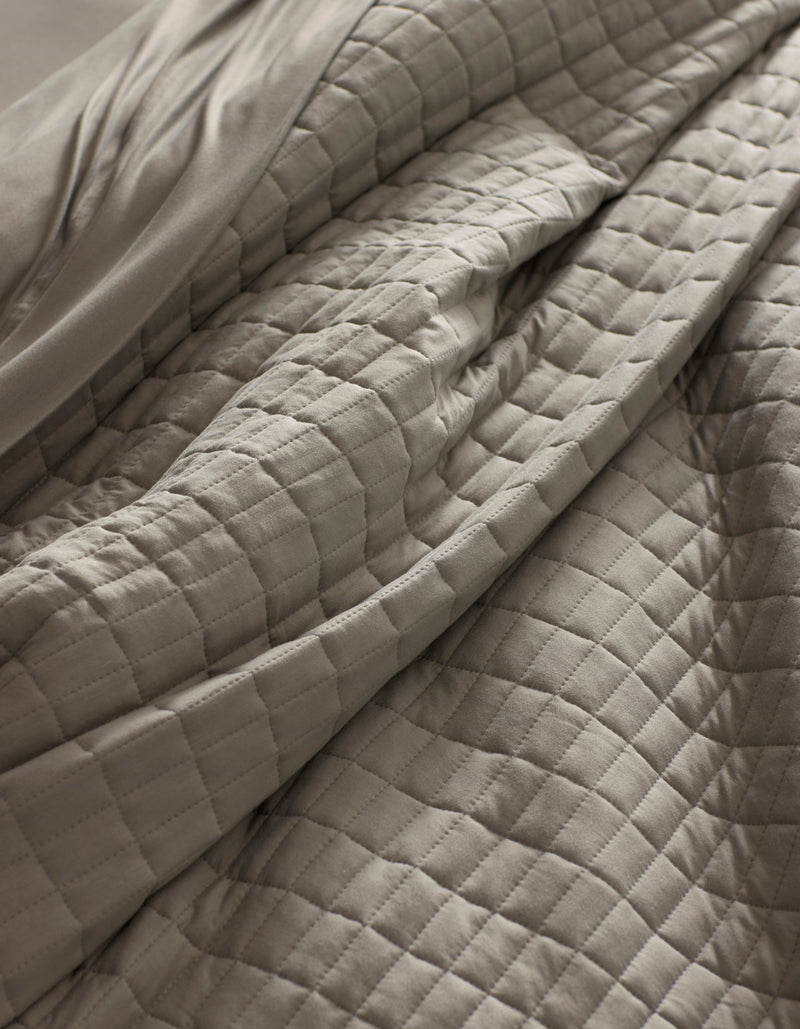 Close-up of the Cozy Earth Bamboo Jersey Quilt in light gray, featuring a quilted grid pattern with visible folds and soft texture for a cozy, inviting look.
