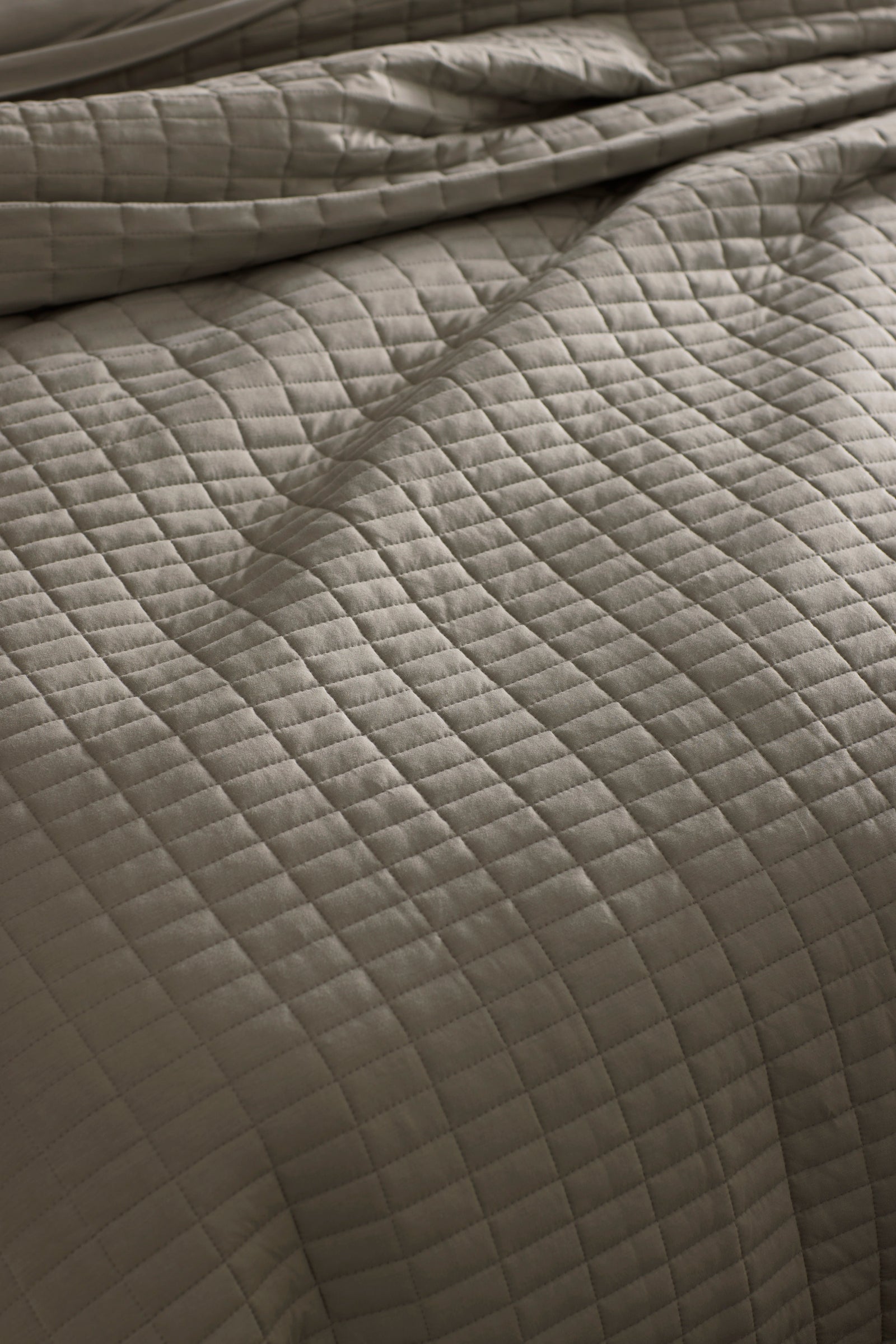 Close-up of a neatly made bed with the Cozy Earth Bamboo Jersey Quilt Bundle, featuring a soft, slightly wrinkled quilt in a light neutral tone with a grid of stitched squares.