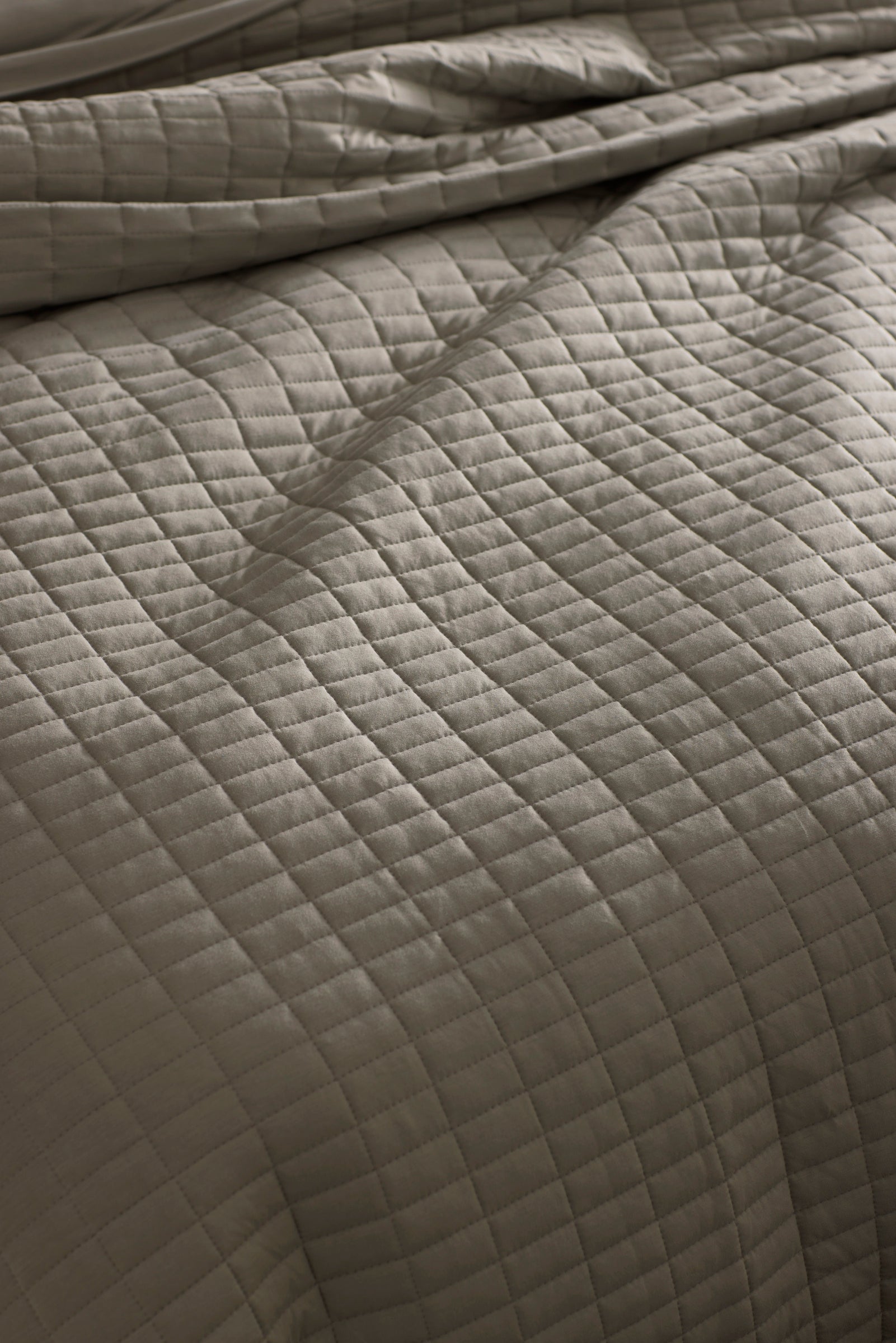 Close-up of a neatly made bed with the Cozy Earth Bamboo Jersey Quilt Bundle, featuring a soft, slightly wrinkled quilt in a light neutral tone with a grid of stitched squares.
