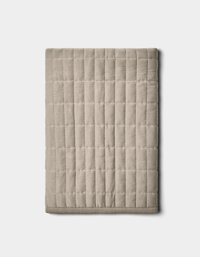 The Bamboo Jersey Quilted Shams by Cozy Earth, shown neatly folded in beige with a grid pattern, are displayed on a plain light background.