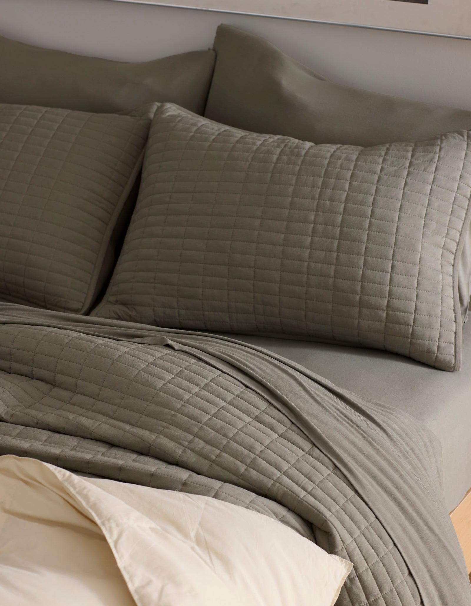 A neatly made bed features Cozy Earth's Bamboo Jersey Quilted Shams in gray, complemented by matching bedding and a light beige sheet partially folded over the quilt for a cozy, inviting look.