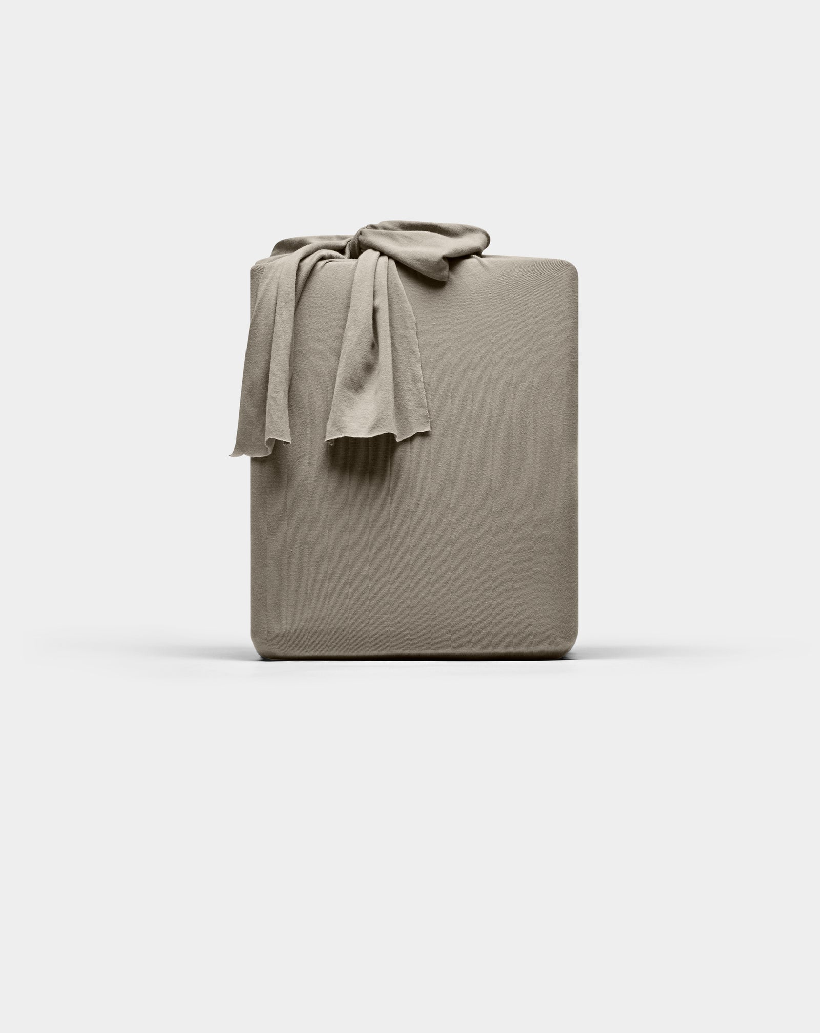 A taupe Cozy Earth Bamboo Jersey fitted sheet is neatly folded with one corner draped over the top, displayed against a plain white background.