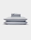 The Cozy Earth Bamboo Jersey Sheet Set is shown neatly stacked with two pillows at the bottom and folded light gray sheets and pillowcases on top, all set against a plain white background.|Color:Shore