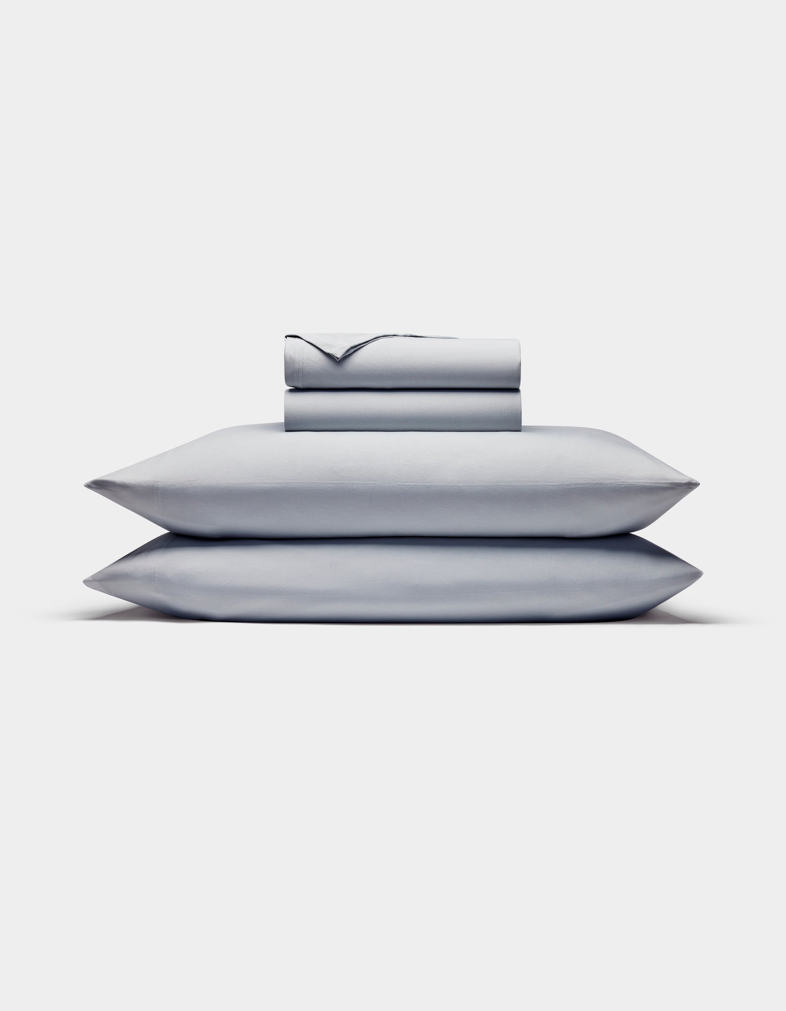 The Cozy Earth Bamboo Jersey Sheet Set is shown neatly stacked with two pillows at the bottom and folded light gray sheets and pillowcases on top, all set against a plain white background.