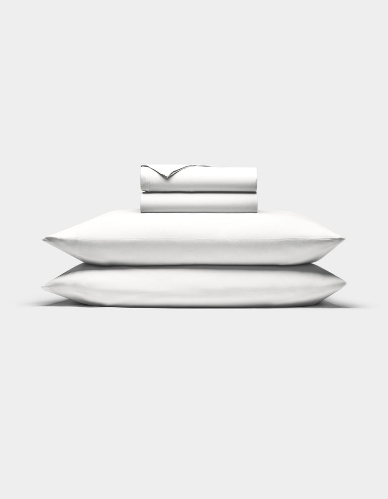 Two white Cozy Earth Bamboo Jersey Sheet Set sheets are neatly folded atop two stacked pillows, all set against a plain white background.