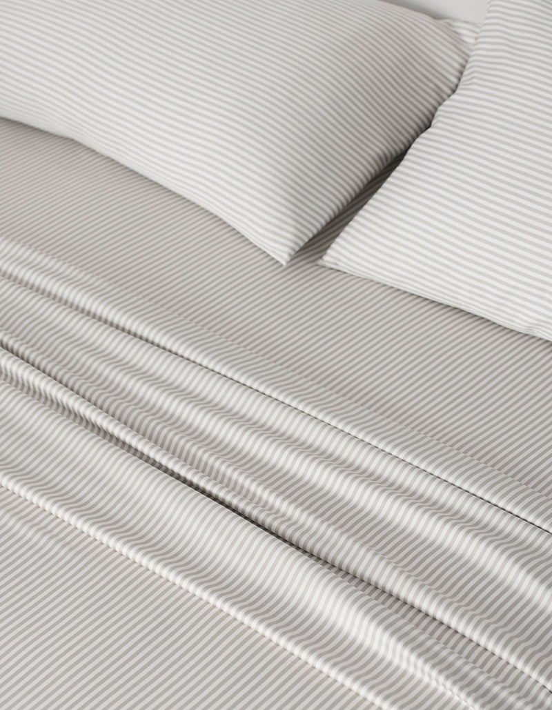 A close-up of a neatly made bed features the Cozy Earth Bamboo Sheet Set—light gray and white thin stripes on sheets and two pillows—offering a soft, orderly look.