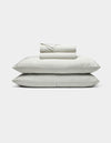 The Bamboo Sheet Set by Cozy Earth features neatly folded white sheets with subtle gray stripes, two stacked pillows, and additional folded sheets, all displayed against a plain white background.|Color:Classic Stripe in Laurel