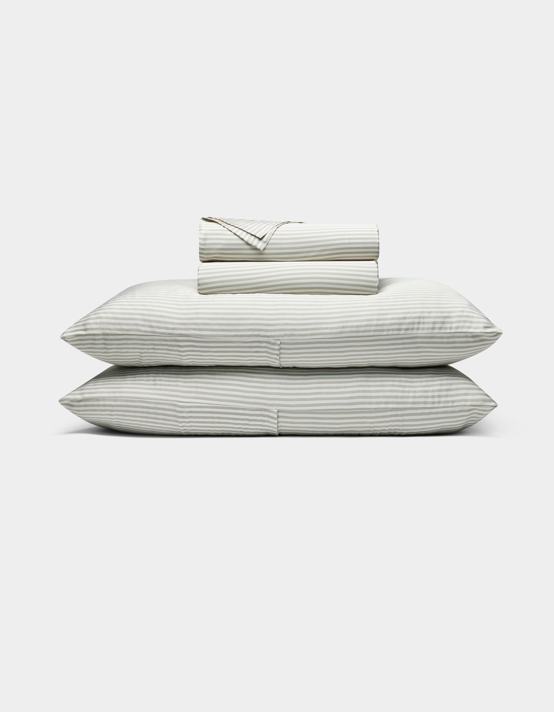 The Bamboo Sheet Set by Cozy Earth features neatly folded white sheets with subtle gray stripes, two stacked pillows, and additional folded sheets, all displayed against a plain white background.|Color:Classic Stripe in Laurel
