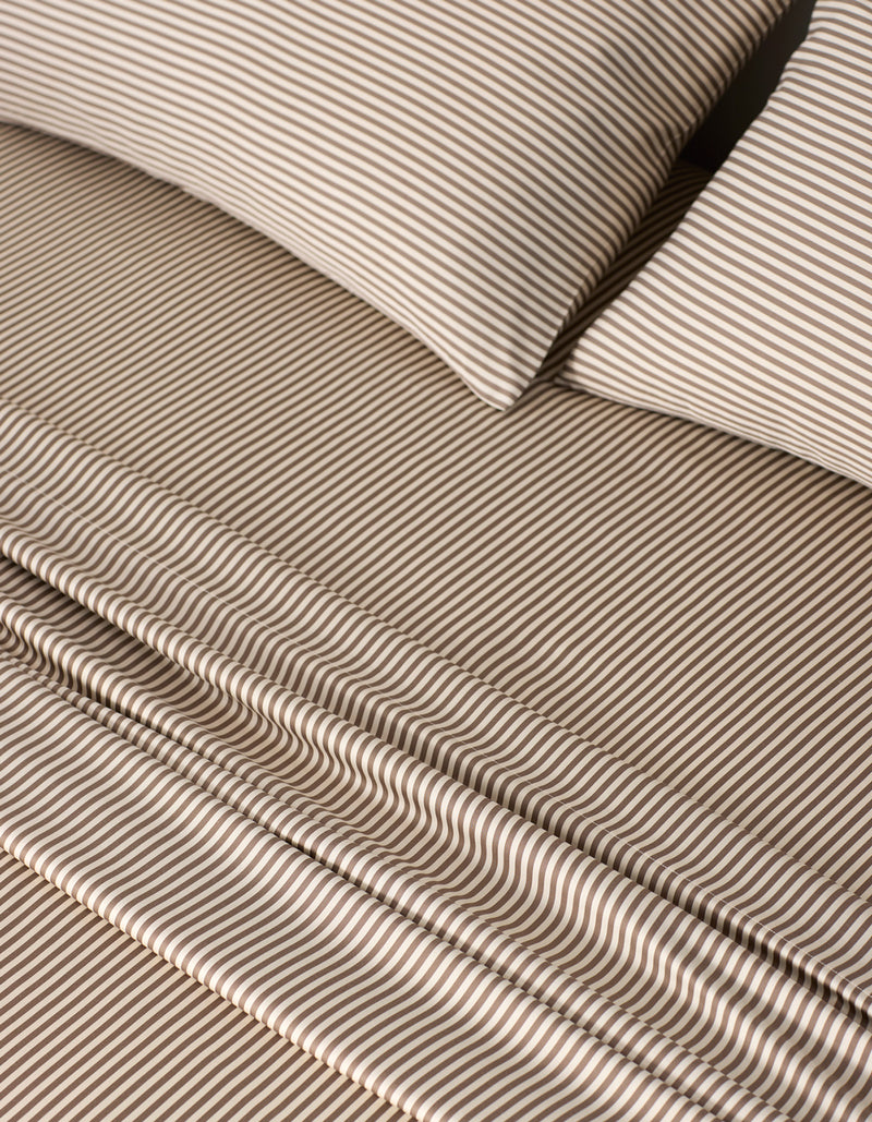 Close-up of a neatly made bed with Cozy Earth Bamboo Sheet Set, featuring matching pillowcases and sheets in a thin brown and white striped pattern. The smooth, soft fabric creates a tidy, inviting look.